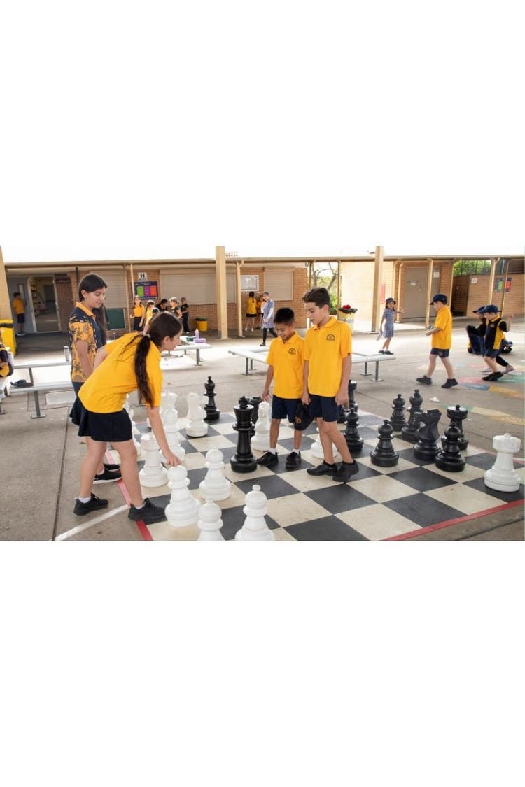 Students playing outdoor chess in playground.